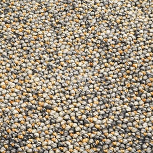 Puede incluir: Una alfombra compuesta por numerosas bolas de lana afieltrada peque&ntilde;as y muy juntas en una paleta de colores variados de gris carb&oacute;n, gris claro, crema y amarillo mostaza, creando una superficie densa y texturizada con un patr&oacute;n esf&eacute;rico.