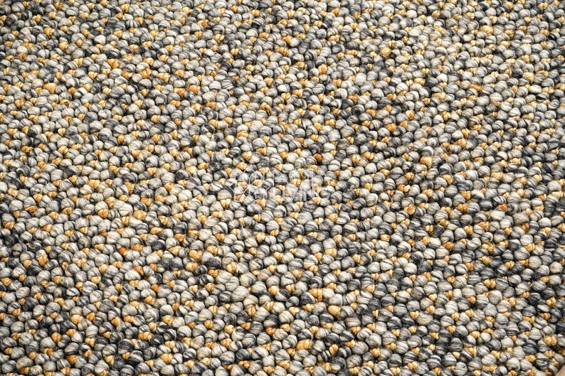 Puede incluir: Una alfombra compuesta por numerosas bolas de lana afieltrada peque&ntilde;as y muy juntas en una paleta de colores variados de gris carb&oacute;n, gris claro, crema y amarillo mostaza, creando una superficie densa y texturizada con un patr&oacute;n esf&eacute;rico.