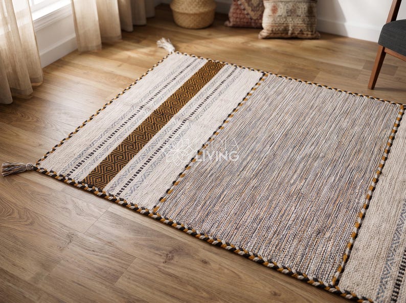 May include: A rectangular area rug featuring a mix of textures and patterns. One section displays a brown diamond motif on a cream background, while the other is a textured grey weave. The edges are finished with a braided border and corner tassels.