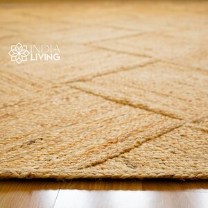 May include: A natural fiber rug with a woven pattern in a light brown color. The rug has a frayed edge and is made of jute.