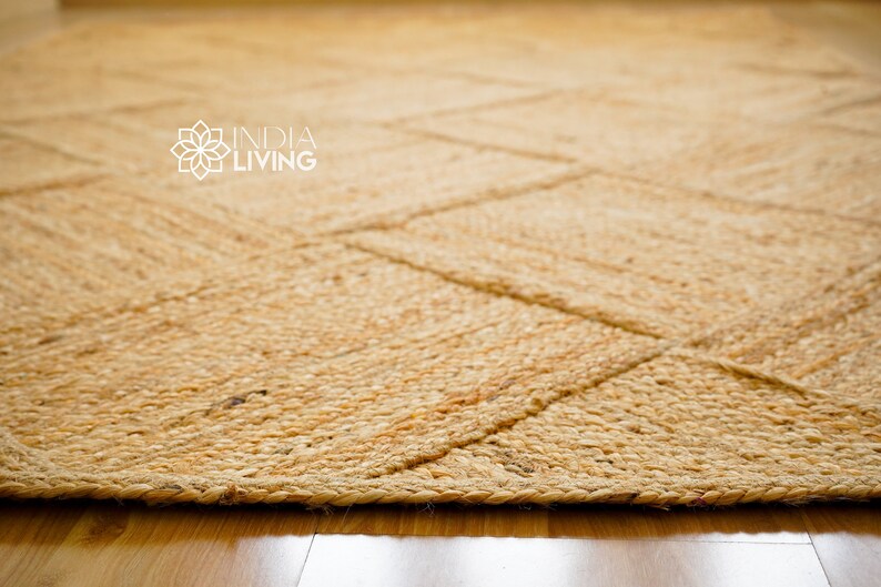 May include: A natural fiber rug with a woven pattern in a light brown color. The rug has a frayed edge and is made of jute.