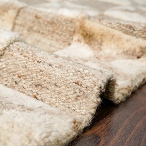 May include: Close-up of a beige and white woven rug with a textured surface. The rug is folded and the edges are visible.