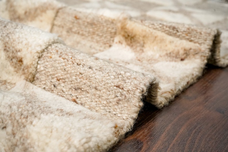 May include: Close-up of a beige and white woven rug with a textured surface. The rug is folded and the edges are visible.
