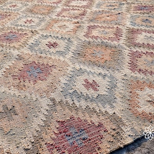 May include: A close-up of a woven rug with a geometric pattern in shades of brown, beige, red, and blue. The rug has a distressed, vintage look.