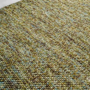 May include: Close-up of a green, blue, and brown textured rug. The rug is made of small, round, woven balls of yarn.