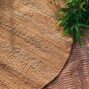 May include: Two woven rugs with a chevron pattern. The rug on the left is a light brown and cream color. The rug on the right is a darker brown and cream color with a hint of pink.