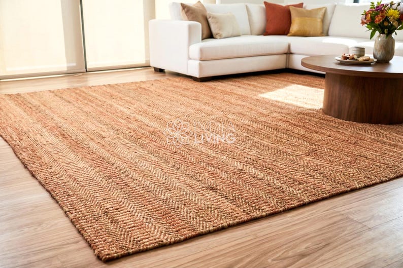 May include: A large rectangular area rug featuring a natural tan and brown woven texture with a consistent herringbone pattern throughout. The rug is laid flat on a light-colored wooden floor, displaying a dense, fibrous weave and earthy tones.