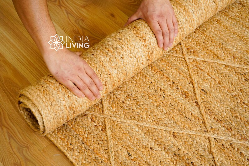 May include: A person rolls up a natural fiber rug with a diamond pattern. The rug is made of jute and has a light brown color.