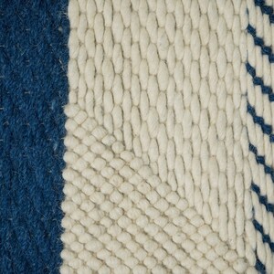 May include: Close-up of a woven rug with a white background and blue stripes. The rug has a textured, hand-woven look.
