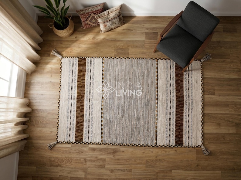 May include: A rectangular area rug featuring a central gray panel flanked by cream and dark brown striped sections with geometric patterns. The rug has tassels at each corner and displays the text INDIA LIVING in the center.