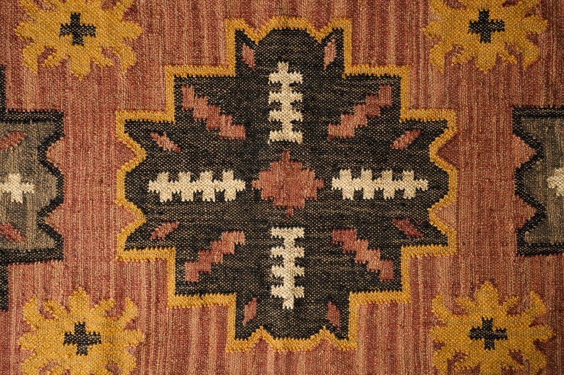 May include: A close-up of a brown, black, and cream patterned rug with a geometric design. The rug has a woven texture and a traditional style.