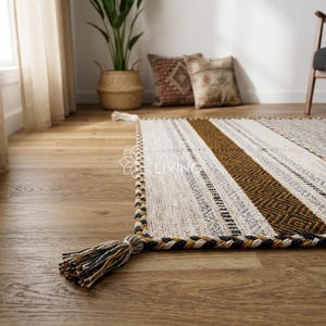 May include: A rectangular area rug featuring a woven pattern of cream, brown, and black stripes with geometric diamond motifs. The rug is finished with a thick, braided border and decorative tassels at the corners in matching earth-tone colors.