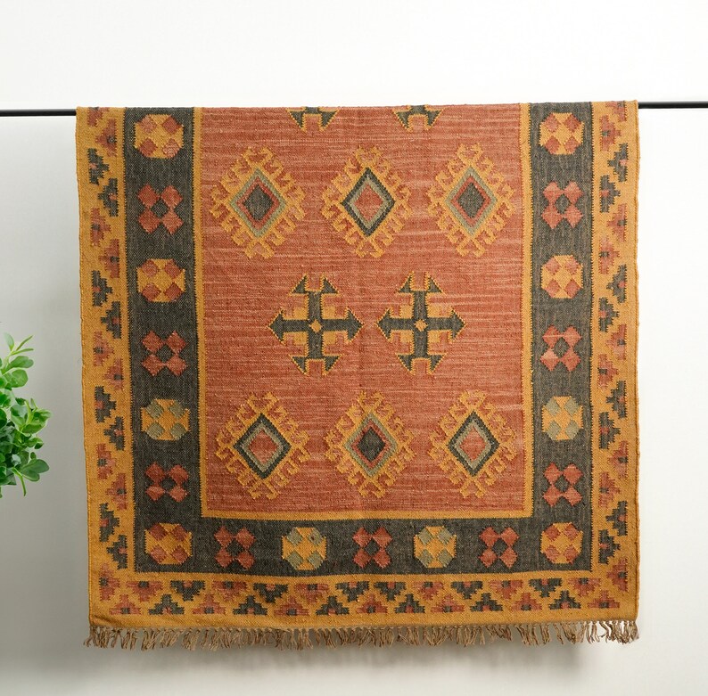 Puede incluir: Una alfombra rectangular con un patr&oacute;n geom&eacute;trico en tonos marrones, naranjas y amarillos. La alfombra tiene un borde con flecos.
