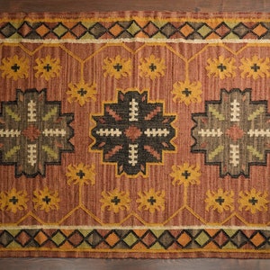 May include: A brown, beige, and green patterned rug with a geometric design. The rug has a fringe border.