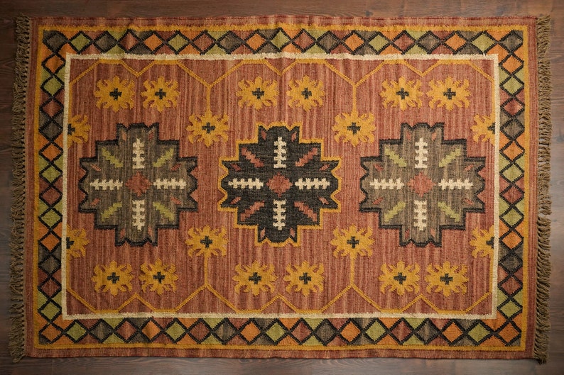 May include: A brown, beige, and green patterned rug with a geometric design. The rug has a fringe border.