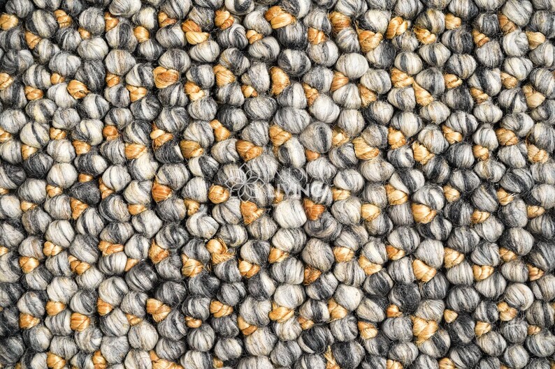 Puede incluir: Una alfombra gruesa y texturizada con un tejido denso de esferas redondeadas similares a la lana fieltrada en tonos gris carb&oacute;n, gris claro y blanco, intercaladas con peque&ntilde;os acentos de fibras de color marr&oacute;n dorado en la superficie.
