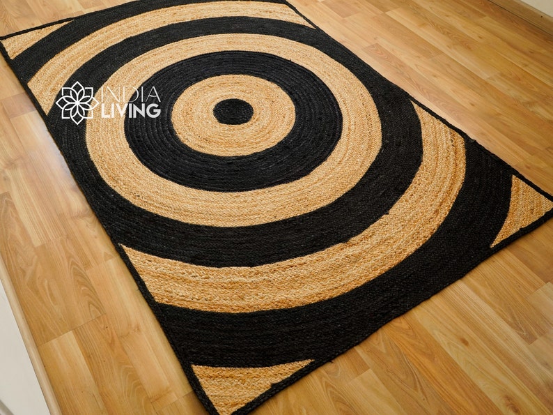 May include: A black and natural jute rug with a large concentric circle pattern. The rug has a modern, geometric design.