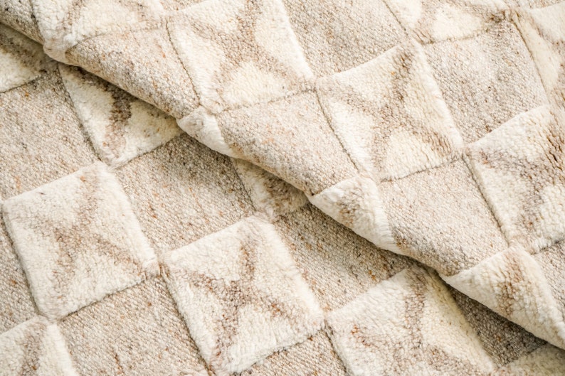 May include: Close-up of a beige and white woven rug with a checkered pattern. The rug has a soft, textured surface.