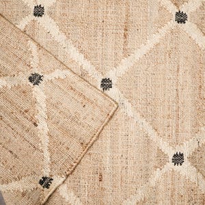 Puede incluir: Primer plano de una alfombra de fibra natural con un patr&oacute;n de diamante y detalles negros. La alfombra est&aacute; hecha de yute y tiene un aspecto natural y terroso.