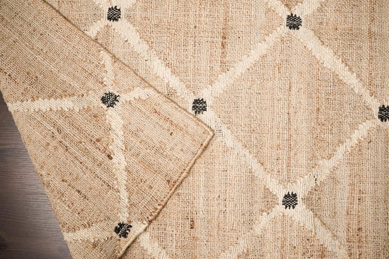 Puede incluir: Primer plano de una alfombra de fibra natural con un patr&oacute;n de diamante y detalles negros. La alfombra est&aacute; hecha de yute y tiene un aspecto natural y terroso.