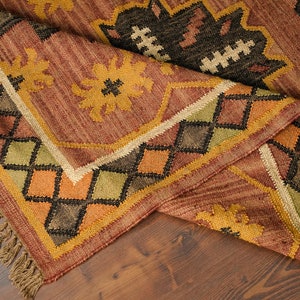 May include: A brown, yellow, green, and black patterned rug with fringe. The rug has a geometric design with diamond shapes and floral motifs.