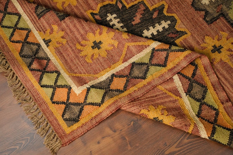 May include: A brown, yellow, green, and black patterned rug with fringe. The rug has a geometric design with diamond shapes and floral motifs.
