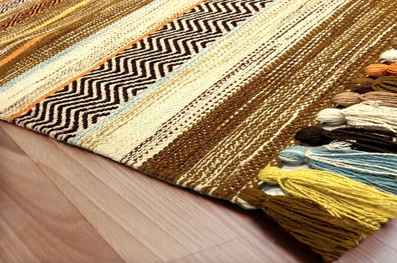 May include: A brown, beige, and orange striped rug with a chevron pattern. The rug has tassels on the end.