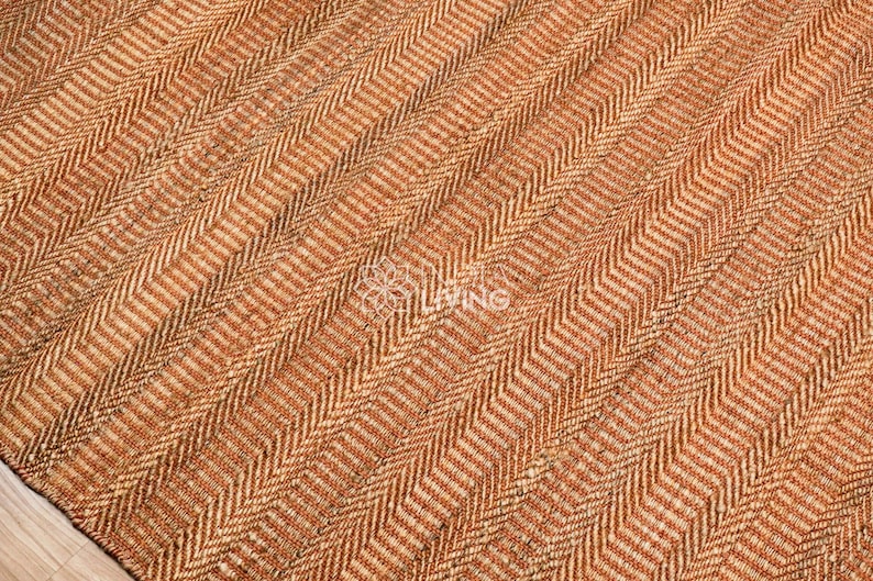 May include: A woven area rug featuring a dense, textured herringbone pattern in alternating shades of warm tan, light brown, and dark brown fibers. The surface displays a consistent, repeating V-shaped weave structure throughout the entire visible area.