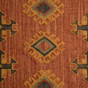 Puede incluir: Primer plano de una alfombra de color rojo, naranja y marr&oacute;n con un dise&ntilde;o geom&eacute;trico. La alfombra tiene una textura tejida y presenta un patr&oacute;n repetitivo de diamantes y cruces.