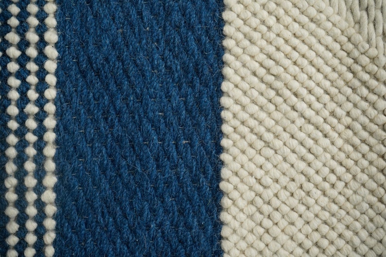 May include: Close-up of a woven rug with a blue and white striped pattern. The rug is made of thick, textured yarn.