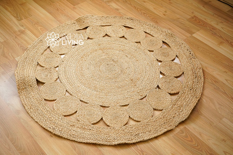 May include: A round, natural fiber rug with a woven design of circles around the outer edge. The rug is made of jute and has a natural, earthy color.