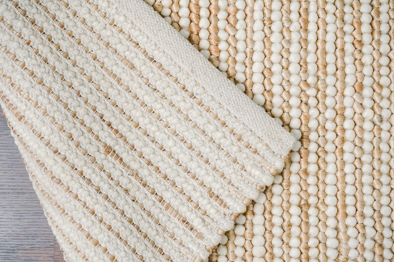 May include: Close-up of a cream-colored woven rug with a textured, bumpy surface. The rug has a striped pattern with alternating rows of small, round bumps and flat woven strands.
