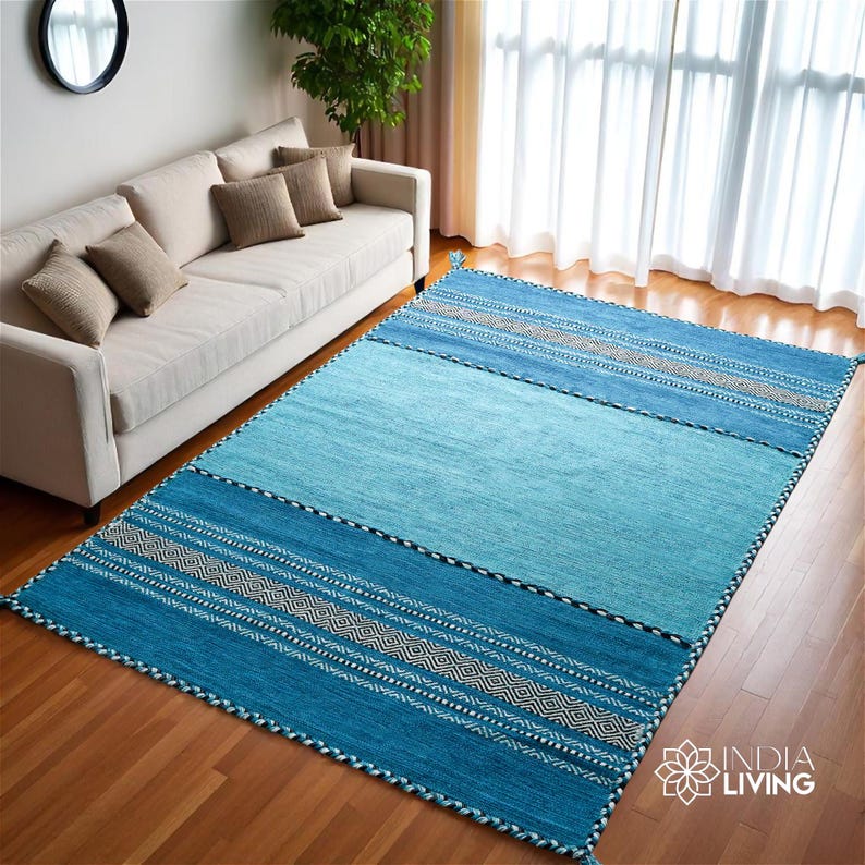 May include: A rectangular area rug featuring a gradient of blue tones, ranging from light sky blue in the center to deep teal at the ends. The rug includes horizontal bands with intricate geometric patterns in white and dark blue, finished with tassels.