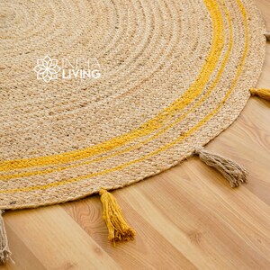 May include: A round jute rug with yellow stripes and tassels. The rug has a natural, earthy look and is perfect for adding a touch of bohemian style to any room.