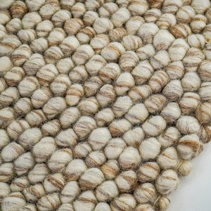 K&ouml;nnte beinhalten: Nahaufnahme eines beige-braunen Wollteppichs aus kleinen, runden Kugeln. Der Teppich hat eine strukturierte, unebene Oberfl&auml;che.