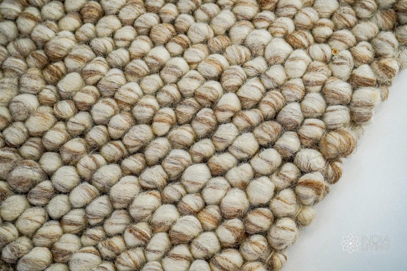 K&ouml;nnte beinhalten: Nahaufnahme eines beige-braunen Wollteppichs aus kleinen, runden Kugeln. Der Teppich hat eine strukturierte, unebene Oberfl&auml;che.