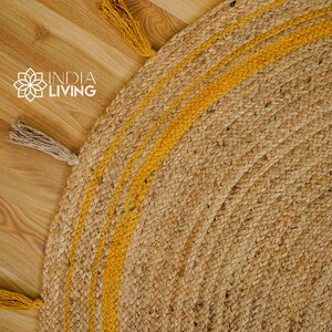 May include: A round jute rug with a natural brown color and yellow stripes. The rug has fringe tassels on the edges.