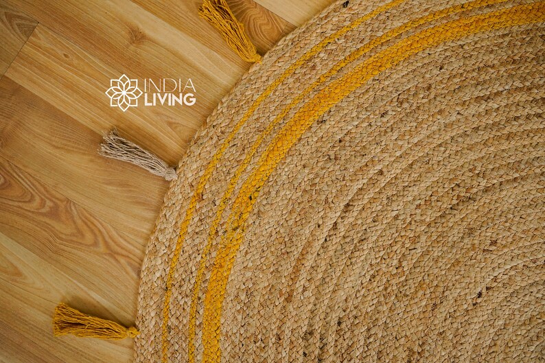 May include: A round jute rug with a natural brown color and yellow stripes. The rug has fringe tassels on the edges.