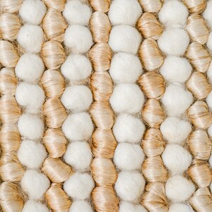 May include: Close-up of a woven rug with a pattern of beige and white yarn balls.