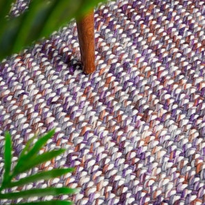 Puede incluir: Una alfombra tejida con un patrón texturizado en tonos de morado, marrón y blanco.