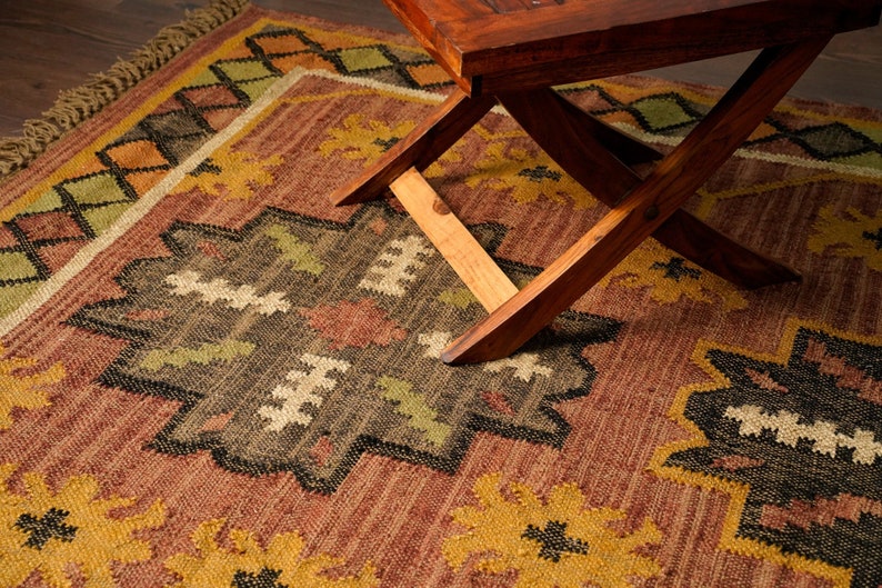 May include: A brown and yellow patterned rug with a wooden folding table on top. The rug has a geometric design with black, green, and white accents.