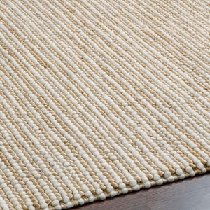 May include: A close-up of a natural fiber rug with a woven texture. The rug has a light brown and white color scheme, creating a striped pattern.