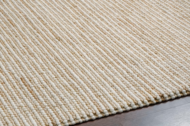 May include: A close-up of a natural fiber rug with a woven texture. The rug has a light brown and white color scheme, creating a striped pattern.