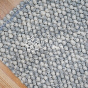 May include: A close-up of a gray and white wool rug with a textured, bumpy surface. The rug is made of small, round balls of wool that are tightly woven together.