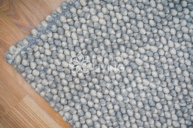 May include: A close-up of a gray and white wool rug with a textured, bumpy surface. The rug is made of small, round balls of wool that are tightly woven together.