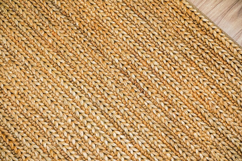 May include: Close-up of a woven rug with a natural, light brown color. The rug has a textured surface with a diagonal pattern. The weave is tight and appears durable, suitable for home decor.