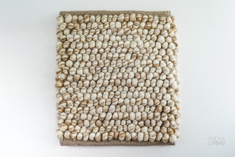 May include: A beige and brown wool rug with a textured, bumpy surface. The rug is made of small, round balls of wool that are woven together.