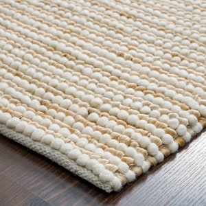 May include: Close-up of a beige and white woven rug with a textured surface. The rug is made of natural fibers and has a subtle pattern.