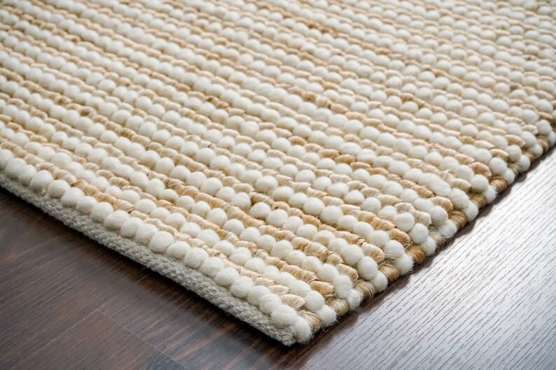May include: Close-up of a beige and white woven rug with a textured surface. The rug is made of natural fibers and has a subtle pattern.