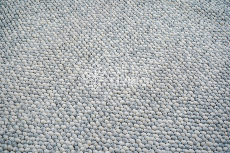 May include: A close-up of a gray and white round rug made of small, round, felt balls. The rug has a subtle pattern of alternating colors.